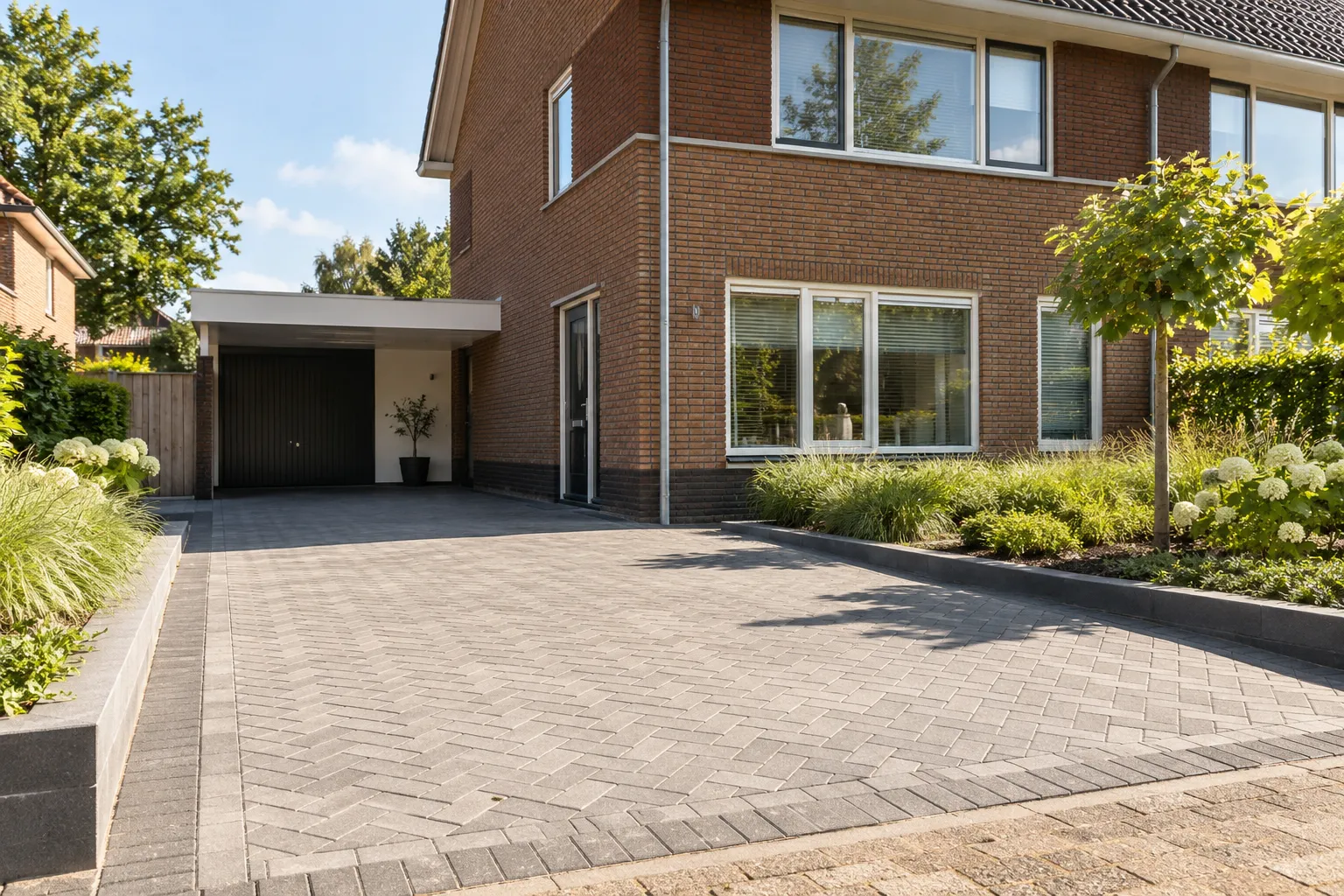 Oprit van grijze klinkers in visgraatverband voor een twee-onder-een-kapwoning met carport